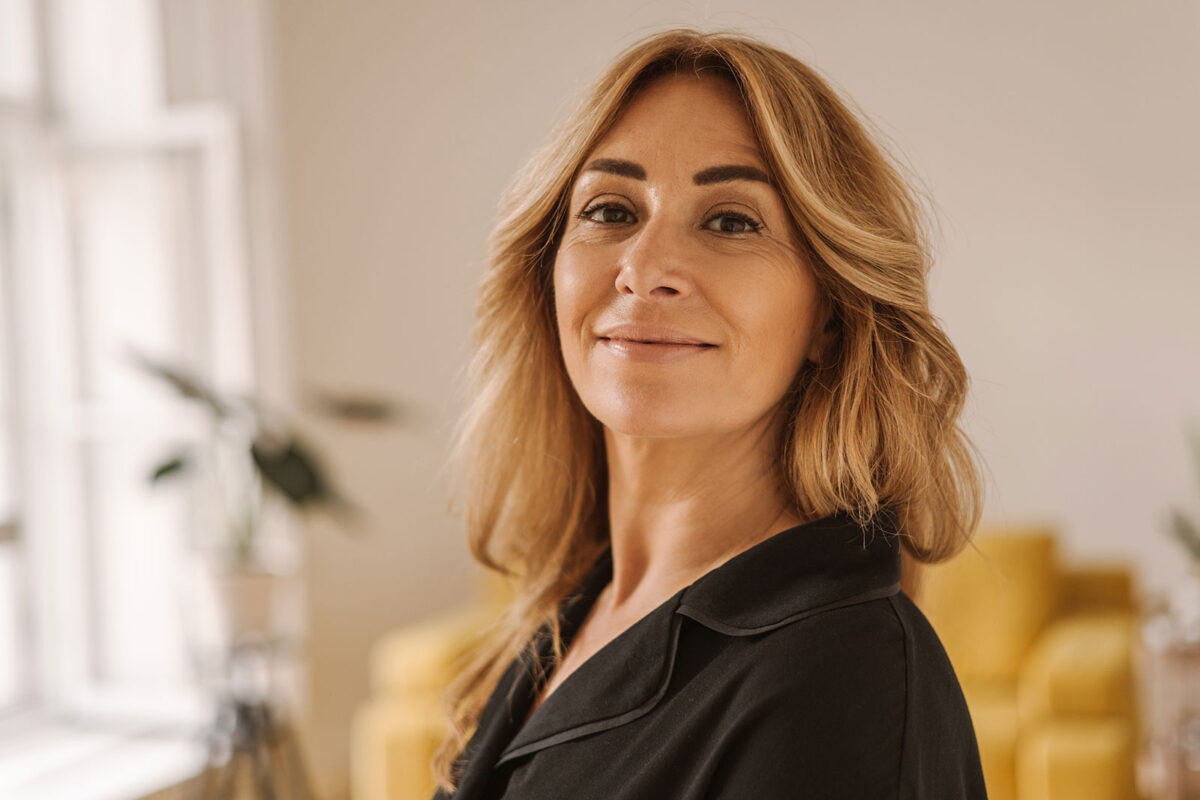 Mulher madura sorridente em ambiente interno, representando a fase da perimenopausa